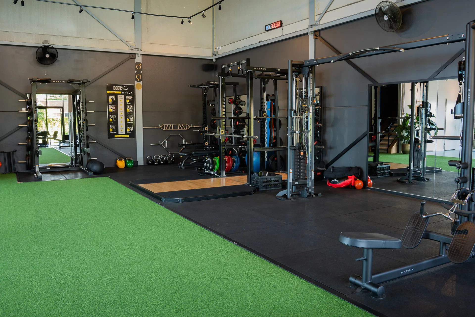 Overzicht van de functionele trainingsvloer met squat racks, kunstgras en Hyrox-zone
