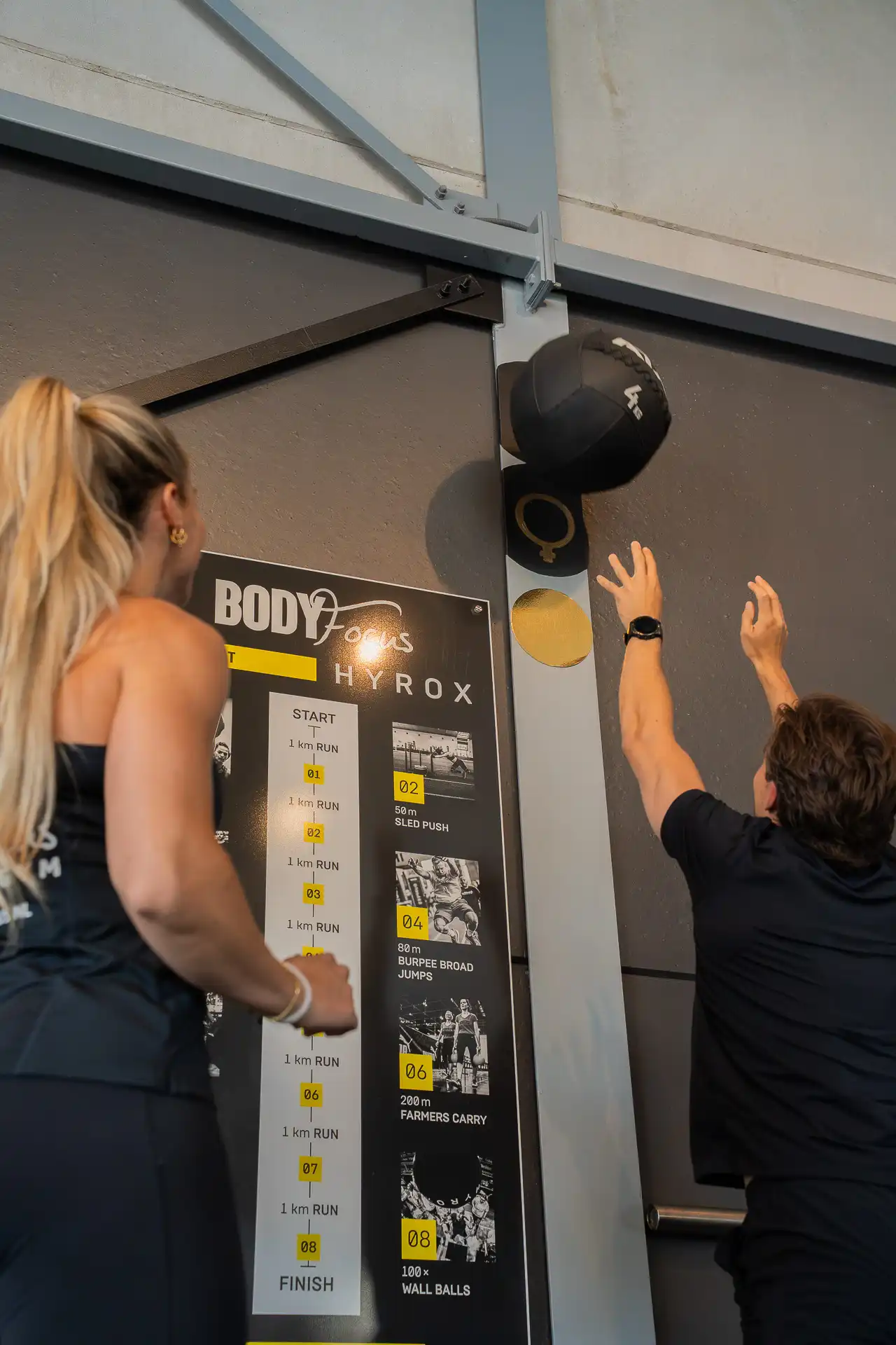 Trainer en member doen wall balls tegen de HYROX-wand bij Body Focus