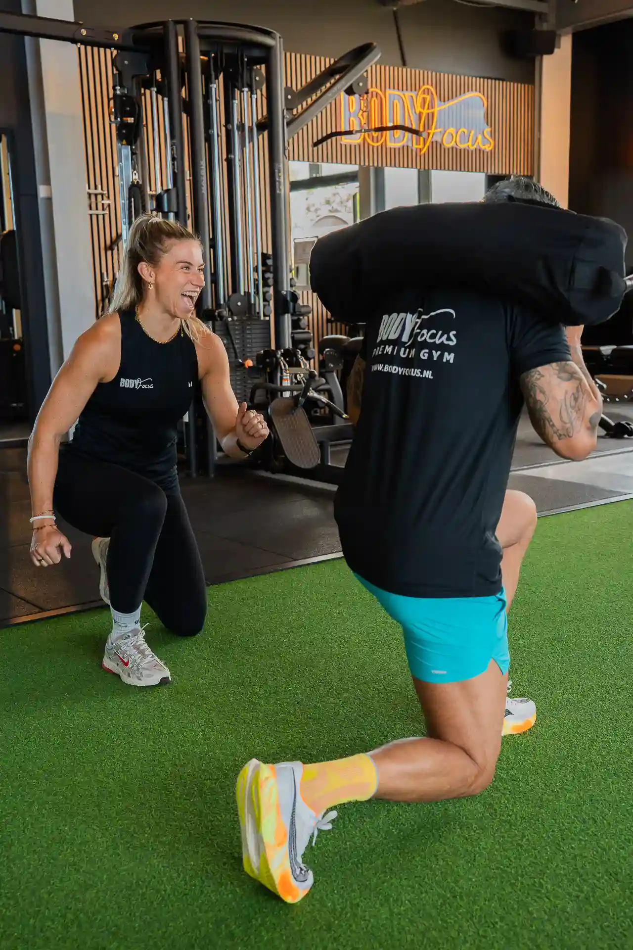 Coach en member trainen samen met sandbag lunges bij Body Focus