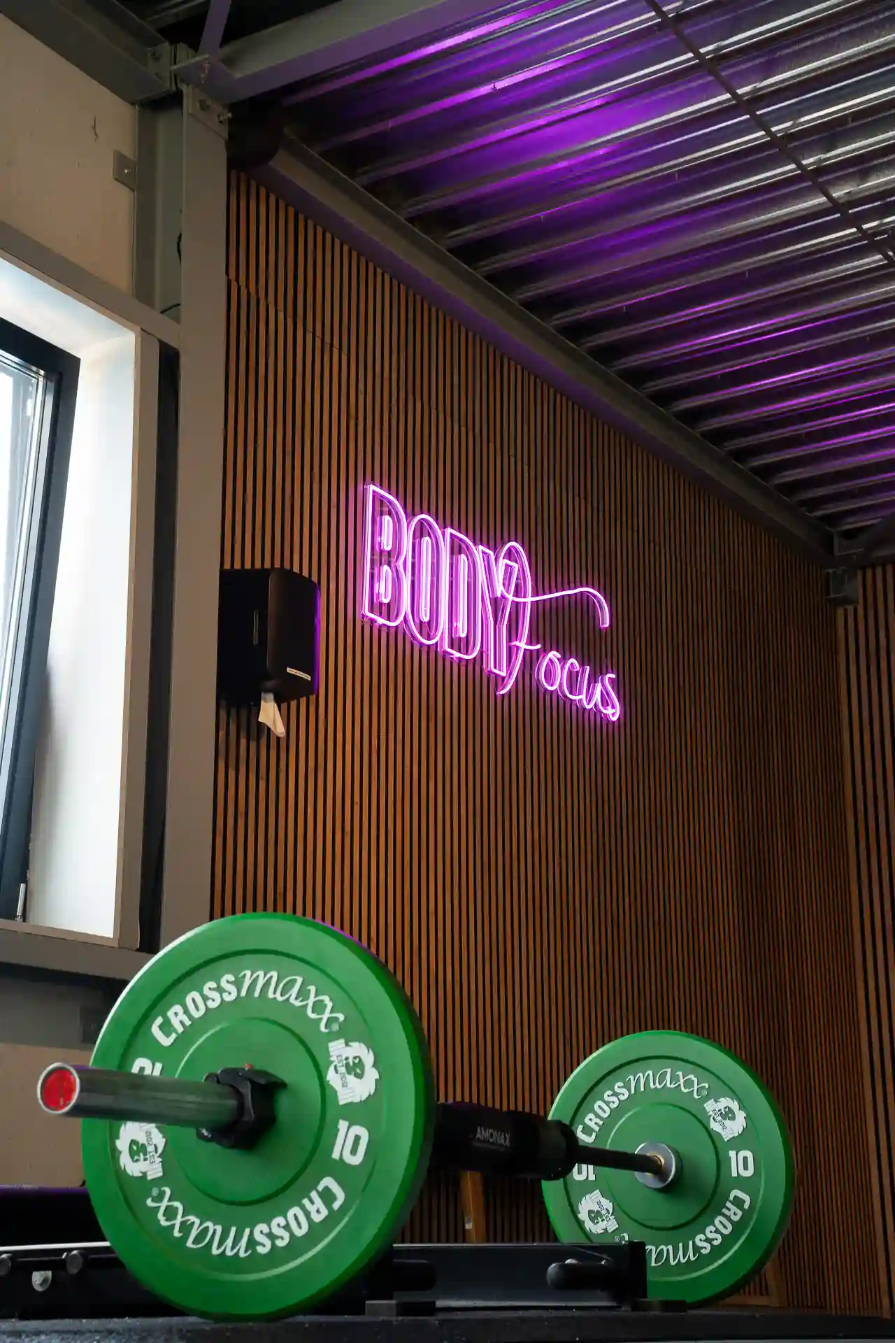 Body Focus neonlogo in paars boven een barbell met groene bumper plates in de Open Gym