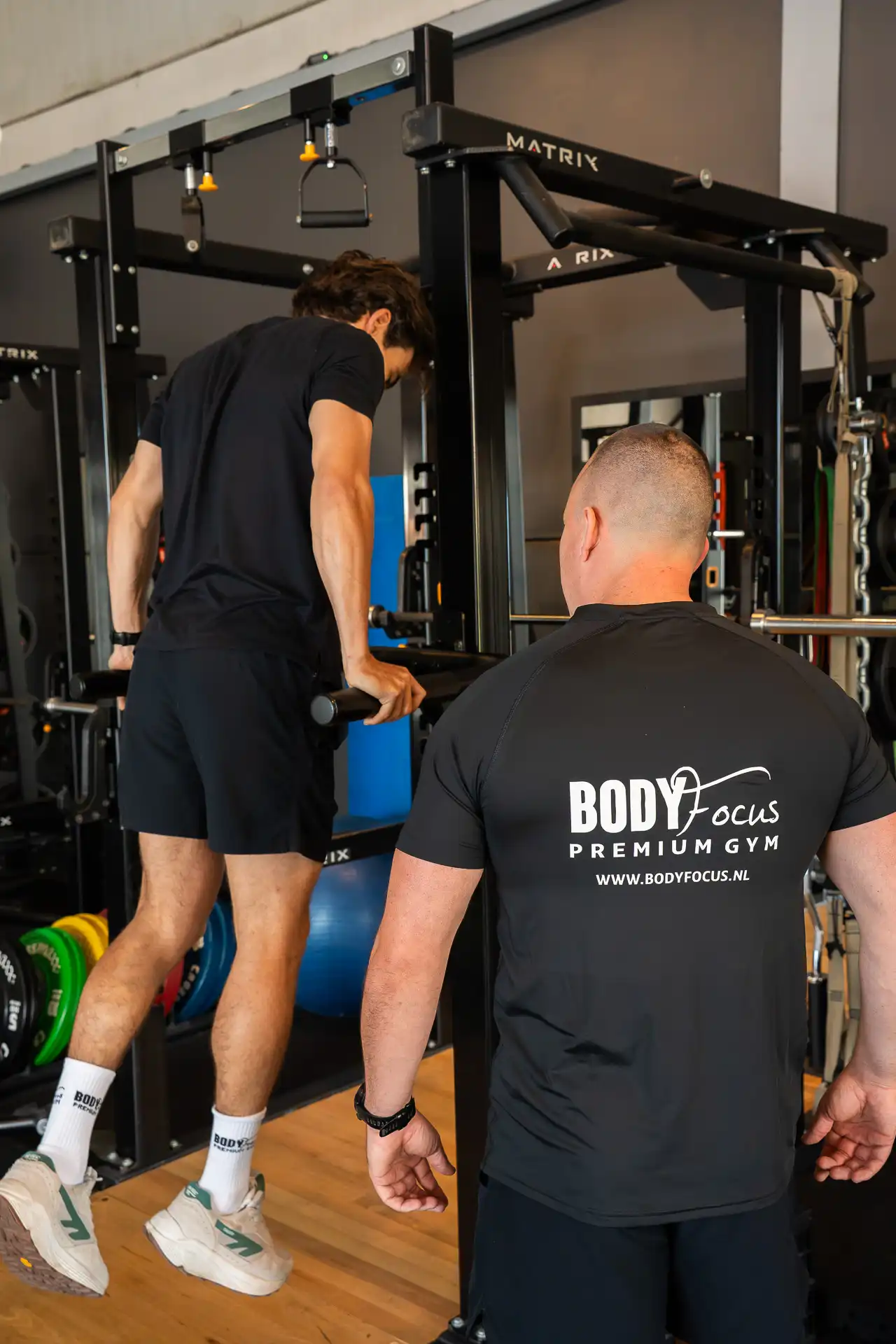 Personal trainer begeleidt member bij pull-up oefening in de multifunctionele rack